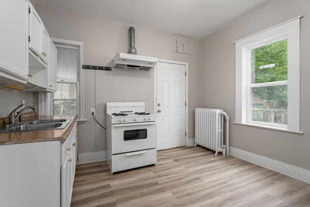 kitchen with white gas range, radiator heating unit, a sink, under cabinet range hood, and white cabinets