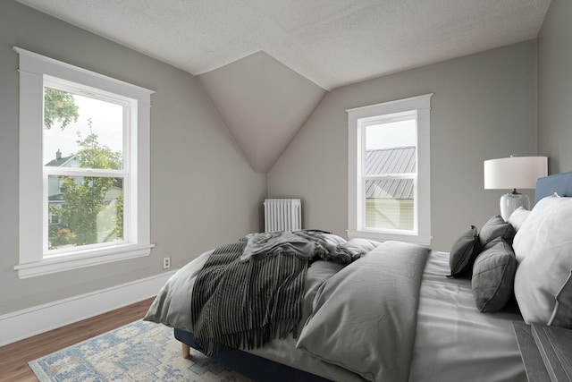 bedroom with radiator, wood finished floors, a textured ceiling, baseboards, and vaulted ceiling