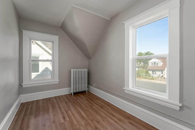 additional living space featuring radiator heating unit, wood finished floors, baseboards, and lofted ceiling