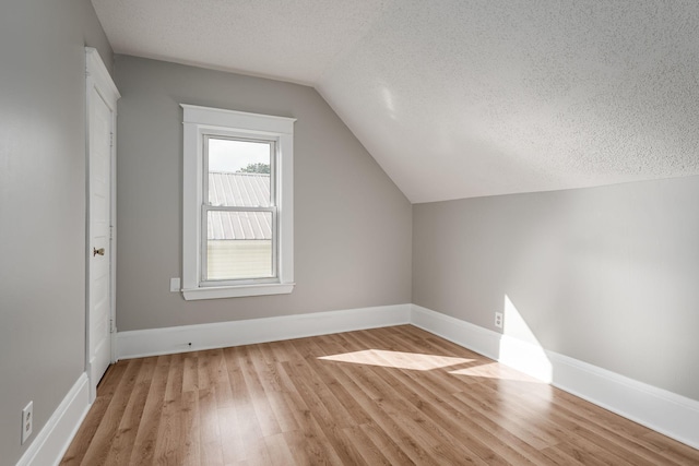 additional living space featuring a textured ceiling, light wood-type flooring, vaulted ceiling, and baseboards