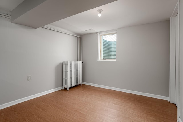 spare room with radiator heating unit, light wood finished floors, and baseboards