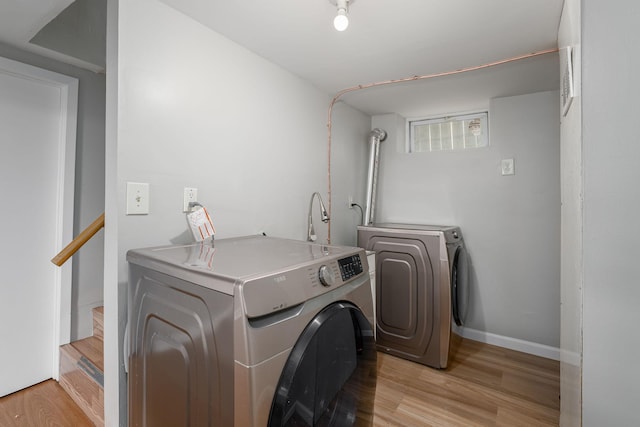 clothes washing area with washing machine and dryer, light wood-style flooring, and baseboards