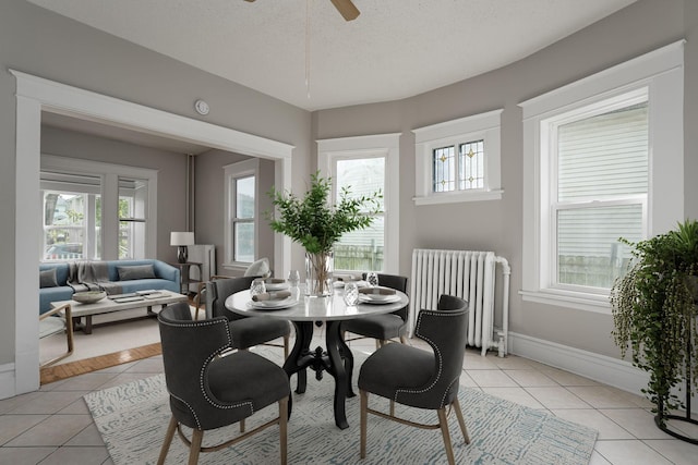dining area featuring radiator, light tile patterned flooring, ceiling fan, a textured ceiling, and baseboards