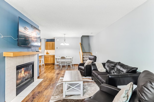 10938 181st Ln NW, Elk River, MN 55330 - living area with light wood-style floors, a chandelier, stairs, a tiled fireplace, and a textured ceiling