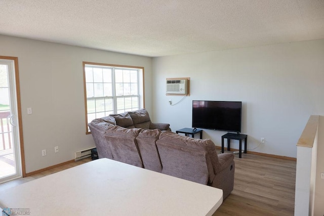 living room with a wall mounted AC, wood finished floors, baseboard heating, a textured ceiling, and baseboards
