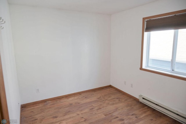 spare room with baseboard heating, light wood-style floors, and baseboards
