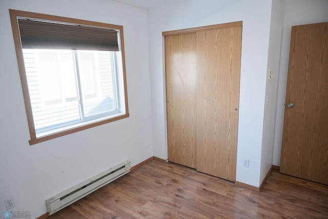 unfurnished bedroom with a baseboard heating unit, a closet, and wood finished floors