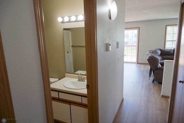 hallway with a sink, light wood-style flooring, baseboards, and a textured ceiling