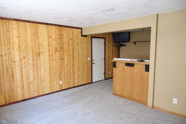 unfurnished living room with wood walls, carpet flooring, a textured ceiling, and baseboards