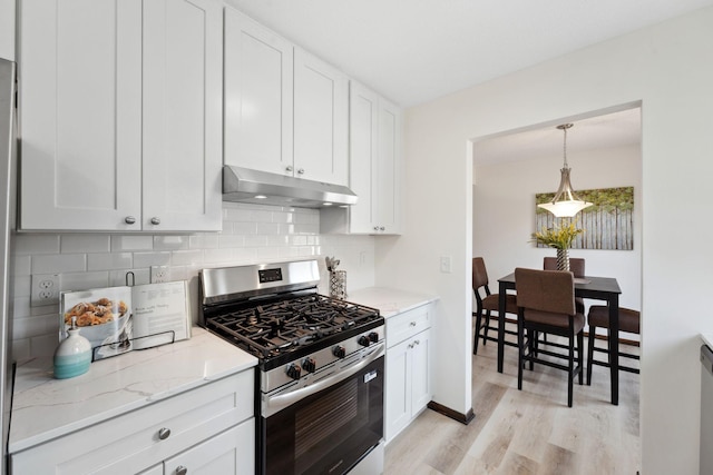 kitchen featuring under cabinet range hood, stainless steel gas range oven, light wood-style flooring, tasteful backsplash, and light stone countertops