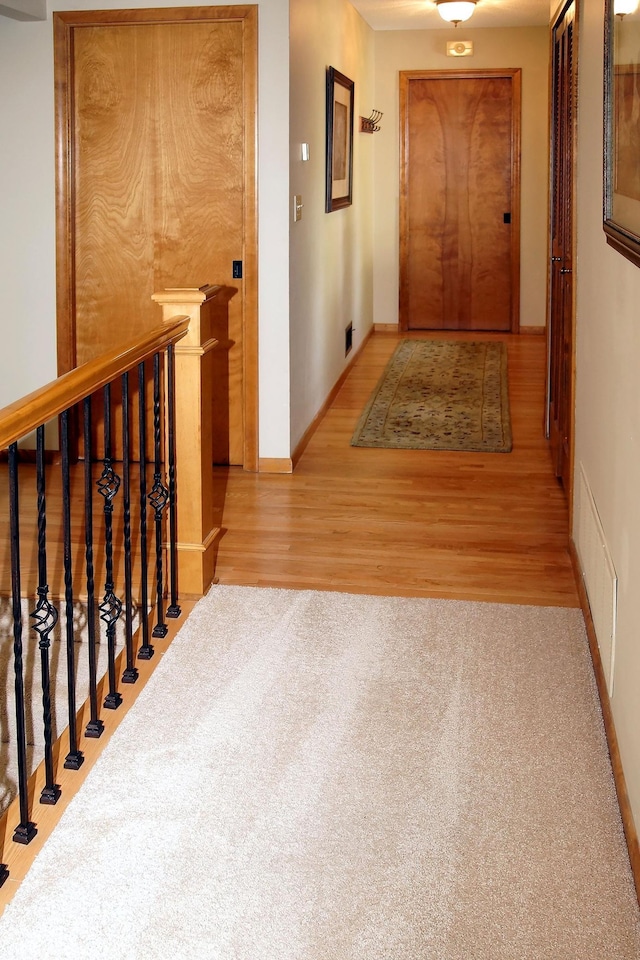 corridor featuring wood finished floors, carpet flooring, baseboards, and an upstairs landing