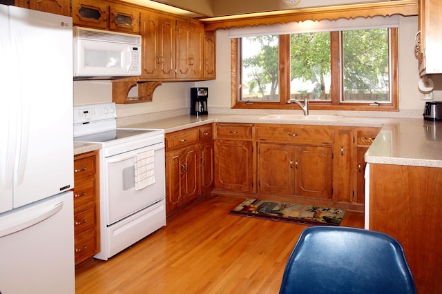 kitchen featuring white appliances, a sink, brown cabinetry, light wood-style floors, and light countertops