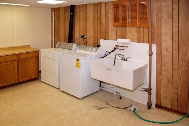 washroom featuring washing machine and dryer, wooden walls, and cabinet space