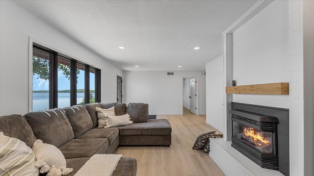 1219 Latoka Dr SW, Alexandria, MN 56308 - living room featuring light wood-style floors, a water view, a textured ceiling, recessed lighting, and a glass covered fireplace