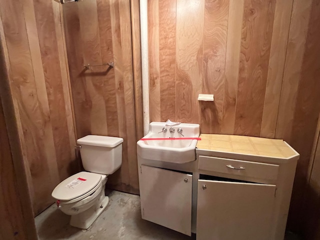 half bath with toilet, unfinished concrete flooring, wooden walls, and vanity