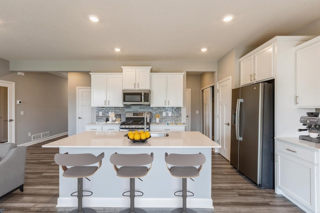 1537 143rd St E, Rosemount, MN 55068 - kitchen featuring appliances with stainless steel finishes, decorative backsplash, a kitchen island with sink, dark wood-style flooring, and light countertops