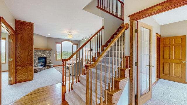 stairway with carpet flooring, a brick fireplace, ceiling fan, baseboards, and wood finished floors
