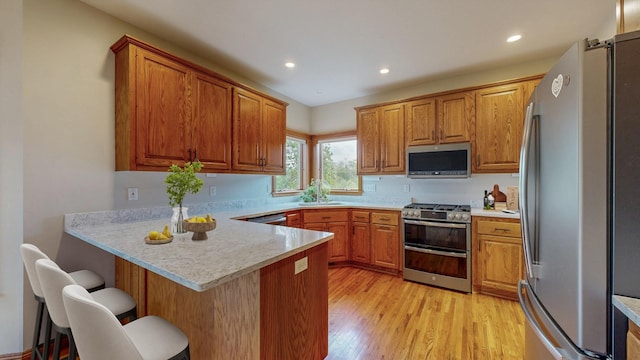 kitchen featuring appliances with stainless steel finishes, a peninsula, brown cabinets, light countertops, and light wood-type flooring