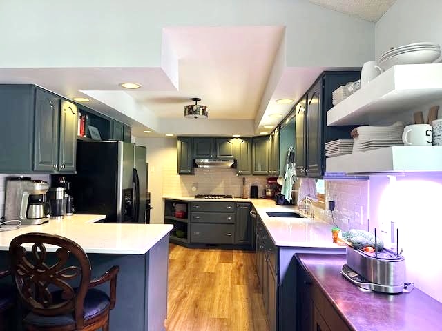 2211 Douglynn Ln, Saint Paul, MN 55119 - kitchen with black fridge, under cabinet range hood, a peninsula, backsplash, and light wood-style flooring