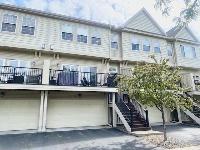 view of property with stairs, an attached garage, and asphalt driveway
