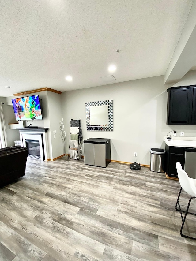 living room featuring baseboards, a glass covered fireplace, a textured ceiling, light wood finished floors, and recessed lighting