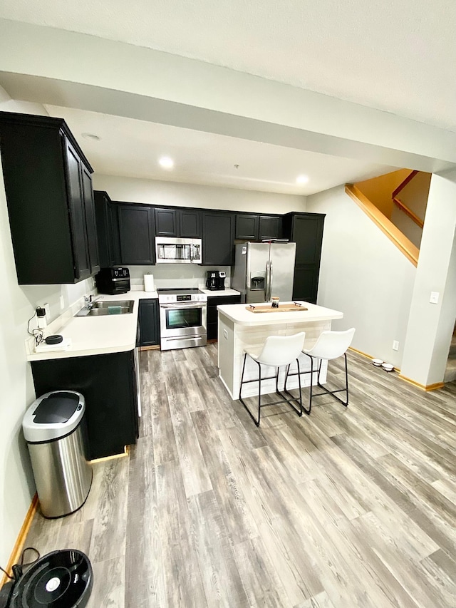 kitchen featuring appliances with stainless steel finishes, dark cabinets, light wood finished floors, baseboards, and light countertops