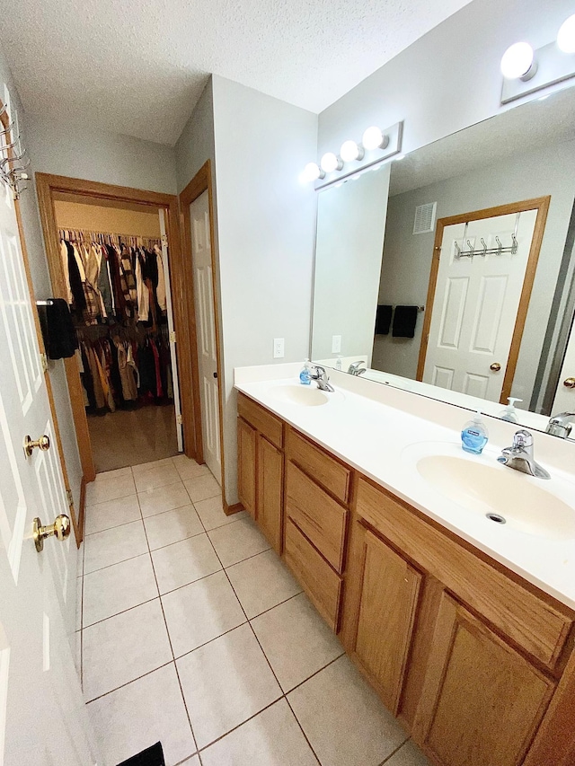 full bath with tile patterned floors, double vanity, a spacious closet, and a textured ceiling
