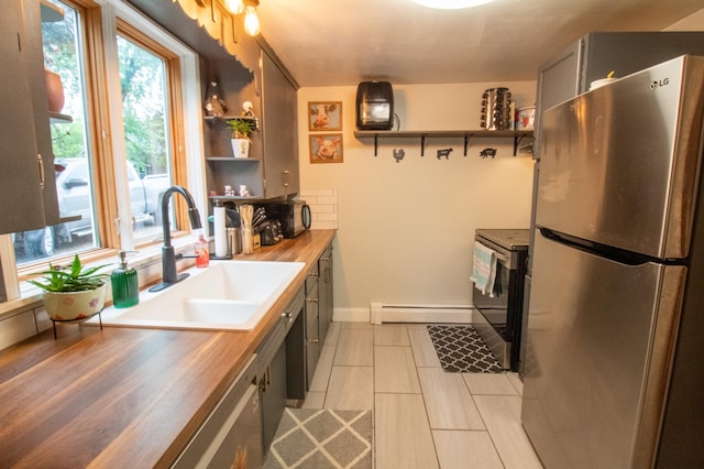kitchen featuring appliances with stainless steel finishes, open shelves, a sink, baseboard heating, and butcher block counters