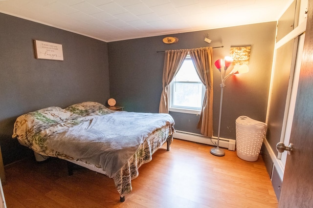 bedroom featuring baseboard heating, ornamental molding, and light wood-style floors