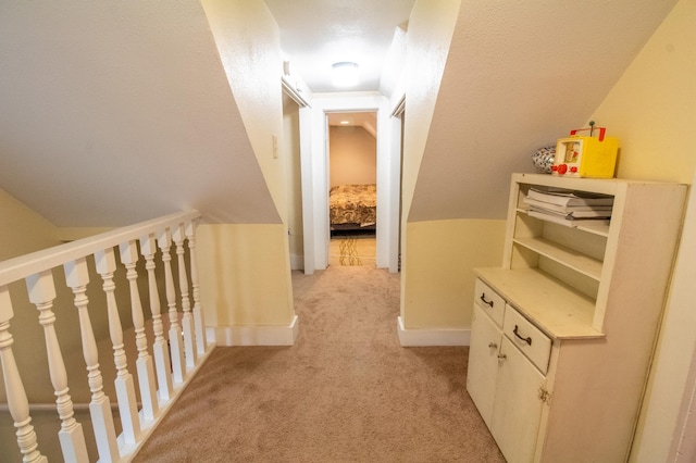 corridor featuring light colored carpet, baseboards, and lofted ceiling
