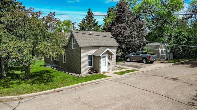view of side of property featuring a storage shed, roof with shingles, an outdoor structure, a yard, and driveway