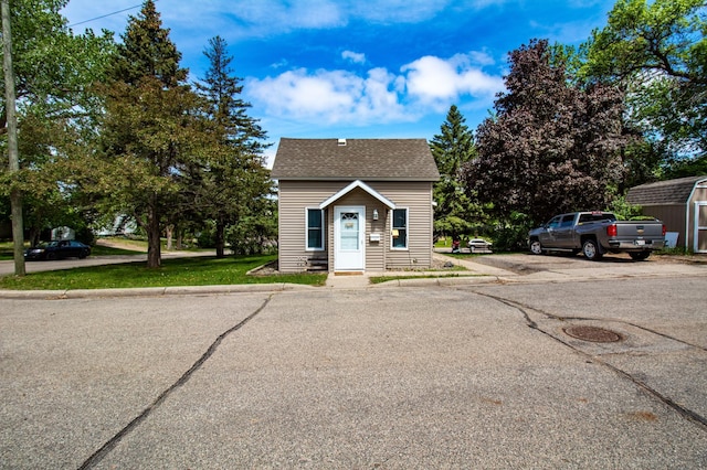 bungalow-style house featuring a storage unit, an outdoor structure, and roof with shingles