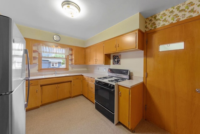 706 9th Ave SW, Faribault, MN 55021 - kitchen with gas range oven, freestanding refrigerator, wallpapered walls, a sink, and light countertops