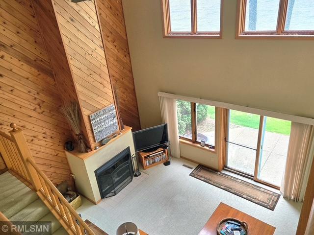 8012 Par Five Dr, South Harbor Twp, MN 56359 - carpeted living room with plenty of natural light, a glass covered fireplace, wood walls, and a high ceiling