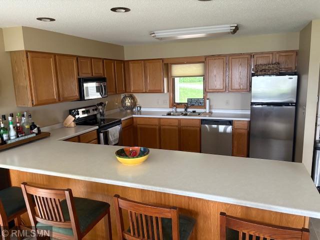 8012 Par Five Dr, South Harbor Twp, MN 56359 - kitchen featuring appliances with stainless steel finishes, a sink, light countertops, a peninsula, and brown cabinets