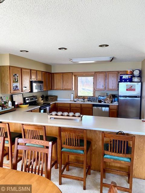 8012 Par Five Dr, South Harbor Twp, MN 56359 - kitchen with stainless steel appliances, brown cabinets, a textured ceiling, a sink, and light countertops