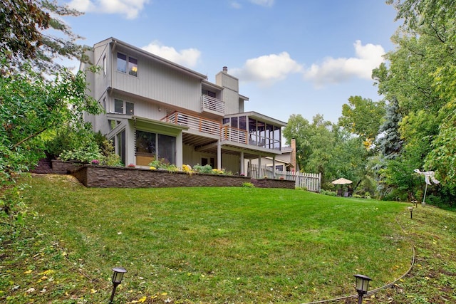 back of house with a balcony, a yard, and a chimney