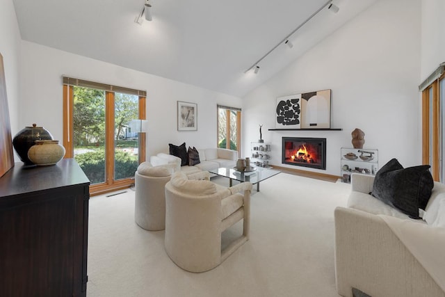 living area featuring track lighting, carpet flooring, lofted ceiling, and a glass covered fireplace