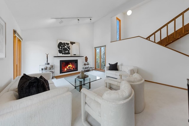living area featuring carpet flooring, a glass covered fireplace, track lighting, and high vaulted ceiling