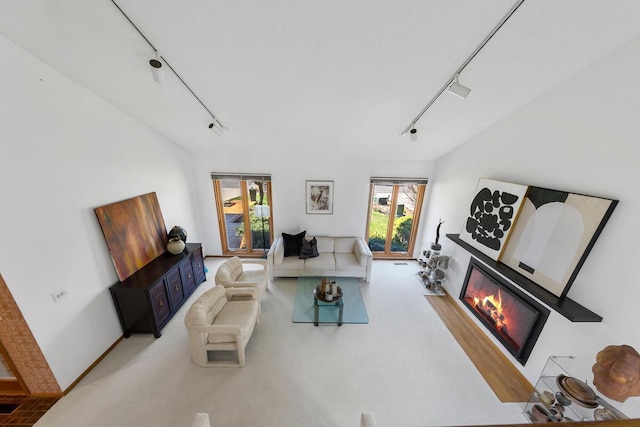 living room with rail lighting, a glass covered fireplace, and light colored carpet