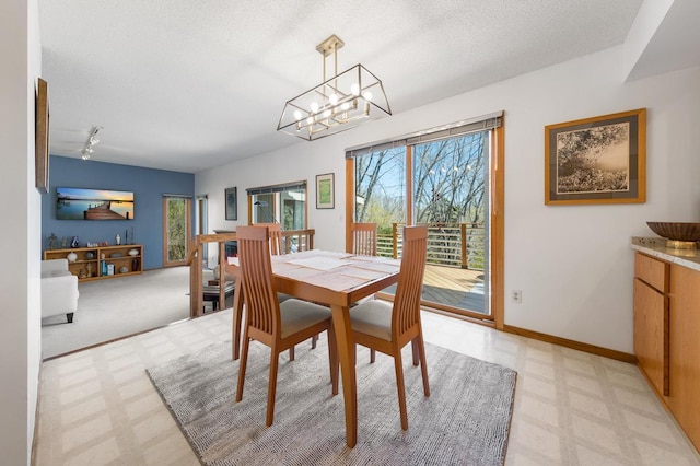 dining room with a chandelier, light flooring, baseboards, and a textured ceiling