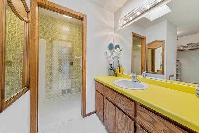 full bath featuring a skylight, tiled shower, vanity, and tile patterned floors