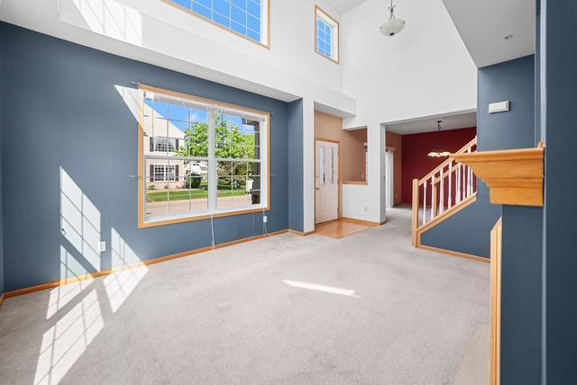11353 Fergus St NE Unit A, Blaine, MN 55449 - unfurnished living room with a towering ceiling, carpet floors, stairs, and baseboards