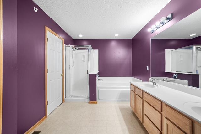 11353 Fergus St NE Unit A, Blaine, MN 55449 - full bathroom with a stall shower, a textured ceiling, a garden tub, double vanity, and baseboards