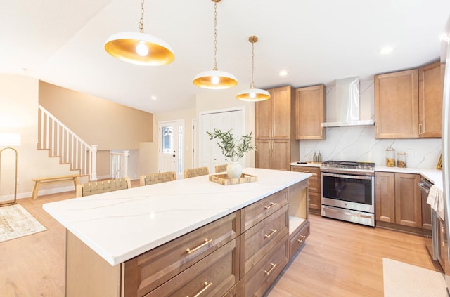 8464 Greenwood Dr, Mounds View, MN 55112 - kitchen with wall chimney range hood, stainless steel range with gas stovetop, light wood finished floors, a kitchen island, and pendant lighting