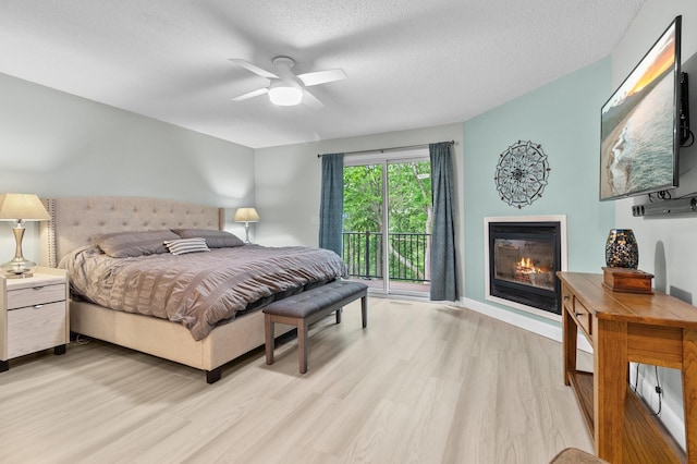 216 Crestview Cir, Jordan, MN 55352 - bedroom with a glass covered fireplace, light wood-style flooring, access to outside, a textured ceiling, and ceiling fan
