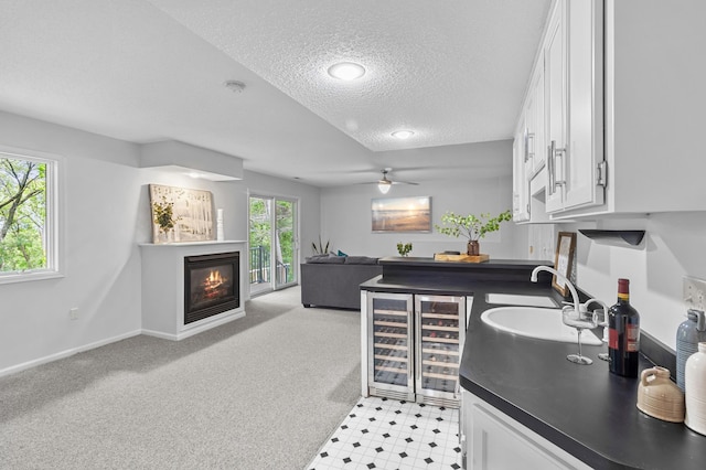 216 Crestview Cir, Jordan, MN 55352 - kitchen featuring wine cooler, a textured ceiling, dark countertops, white cabinetry, and a glass covered fireplace