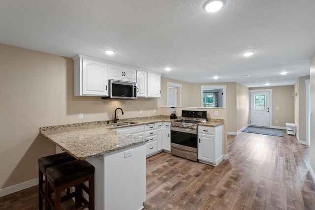 6339 140th Ave SE, Clear Lake, MN 55319 - kitchen with appliances with stainless steel finishes, a peninsula, white cabinets, wood finished floors, and a breakfast bar area