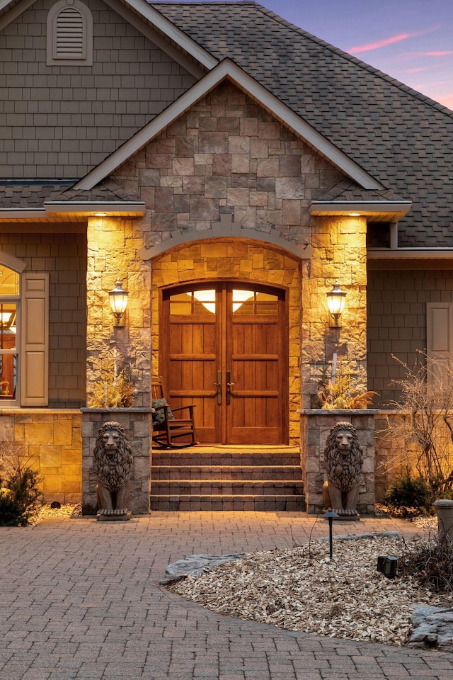 12159 Quail Avenue Ln N, Stillwater, MN 55082 - exterior entry at dusk with a shingled roof, stone siding, and french doors