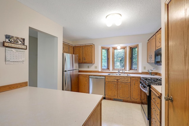 kitchen with appliances with stainless steel finishes, brown cabinetry, a sink, light countertops, and a textured ceiling